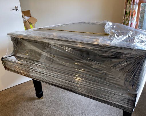 Large ebony piano wrapped in cling film to protect against scratches while being transported